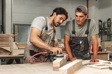 Two young carpenters working with wood standing at table in workshop