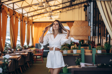Beautiful blonde model woman, fashionable in a white suit, posing in a summer cafe