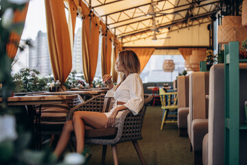 Beautiful blonde model woman, fashionable in a white suit, posing in a summer cafe