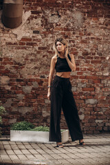 Beautiful blonde model woman, fashionable in a black suit, poses against the walls of a building