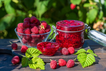 Red raspberry jam and fresh raspberry on a rustic wooden table outdoors near garden. Rustic style, closeup