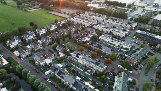 Aerial overview of a beautiful suburban neighborhood with solar panels on rooftops. The sun flares into the camera