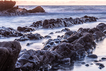 Rocky shore of a coast in the sunset, blurred water by long time exposure