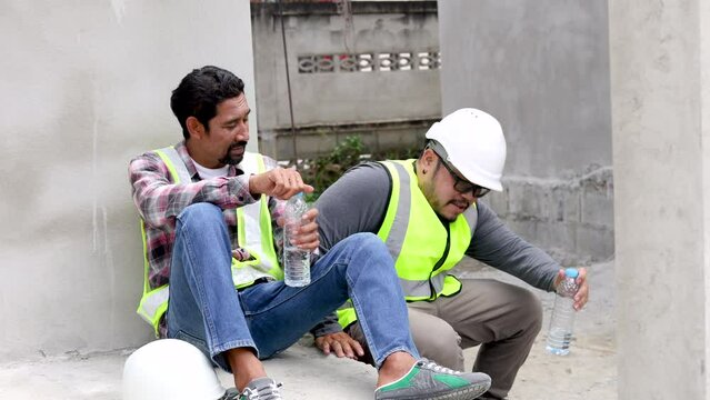 Hopeless middle-aged Indian worker are stressed work hard sweat tired sitting at construction site, Asian foreman colleague give water to laborer man sit together relaxing at lunch break on summer day