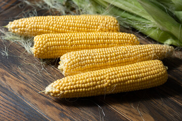 Fresh sweet corns on cobs on rustic wooden table with leaves