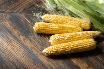Fresh sweet corns on cobs on rustic wooden table with leaves