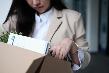 Frustrated fired female employee packing belongings in cardboard box leaving workplace. Unemployment concept