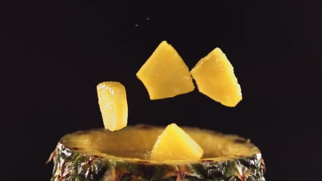 Pineapple pieces falling on the surface of half pineapple in slow motion.
