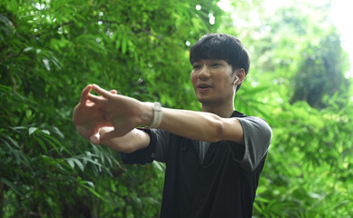 Smiling asian male runner stretching in arms the forest after running. Sports motivation, adventure, healthy lifestyle