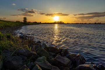 During this beautiful sunset, the stones on the banks of the river De Lek are just lit by the low sun