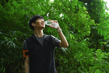 Happy male runner drinking water from a bottle, resting after trail running. Sports, adventure and healthy lifestyle