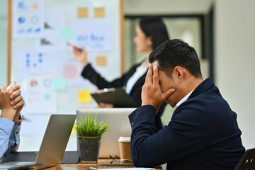 Frustrated tired male employee having problems, feeling tired at corporate meeting. Stress at work and overwork concept