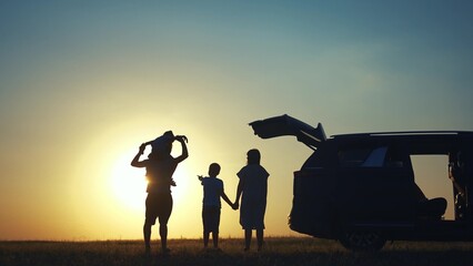family traveling by car. family watching the sunset silhouette next to the car in the park. happy...
