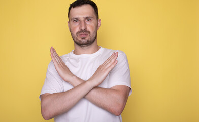 Man isolated on yellow background making stop gesture x crossing hands palms arms.