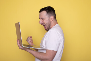 Happy man winner winning online watching game on laptop screaming about goal win celebrating great prize isolated on yellow background.