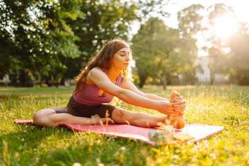 Fitness woman doing yoga, sports exercises in the park. Athletic woman sitting on a mat outdoors on a sunny lawn. Fitness. Active lifestyle.