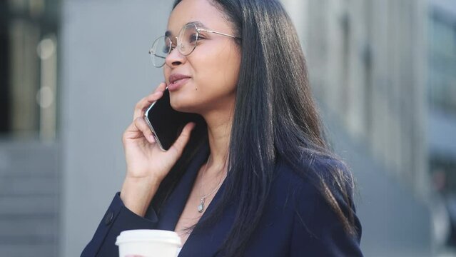 Successful confident businesswoman talking on mobile phone has working or personal conversation while has break at office centre Positive worker employee with cup of coffee using smartphone outdoors