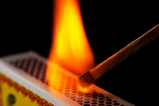 A matchstick lights after it is struck agains the flint surface of a match box. Everything is real, no flame filters.