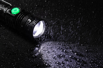LED Flashlight water resistant in drops and rain on black background