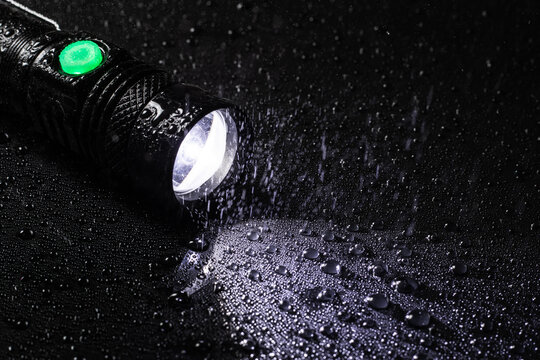 LED Flashlight water resistant in drops and rain on black background