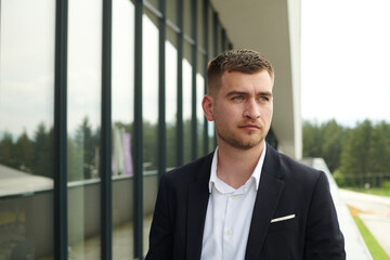 Fototapeta premium A CEO dressed in a sleek black suit stands confidently at the entrance of a modern corporate building, awaiting the start of the workday in the bustling urban environment.