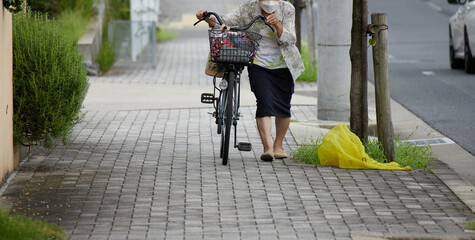 住宅地の道路で自転車を押して歩くシニア女性の姿