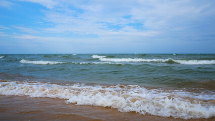 Calm sea with a sandy beach against a blue sky. Waves with foam roll to the shore