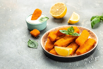 Crispy breaded deep fried fish fingers with breadcrumbs served with sauce and lemon. Food recipe background. Close up