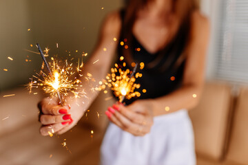 A young girl with beautiful well-groomed hands holds burning sparklers. Girl's hands and New Year's lights close-up. New Year and Christmas background.