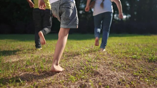 a group of children run in the park on the grass. happy family kid dream concept. children with bare feet run on the grass in the park at sunset. bare feet group of kids run lifestyle in the park