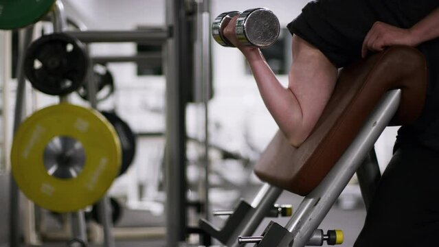 A man doing dumbbell bicep curls on an preacher bench with a light weight using right arm