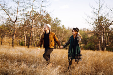 Stylish woman and a man are relaxing in nature. Couple in love enjoying time together while walking at sunset in autumn. Concept of people, style, love, relaxation.