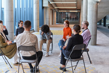 A diverse group of young business entrepreneurs gathered in a circle for a meeting, discussing corporate challenges and innovative solutions within the modern confines of a large corporation