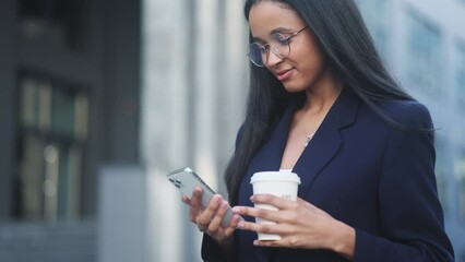Successful young businesswoman with cup of coffee hold smartphone scrolling social media texting browsing online checking email during break at work in modern business centre - Powered by Adobe