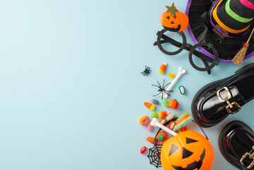 Playful Halloween night revelry for children concept. High-angle shot showcasing treats, child's costume details and spooky embellishments on blue isolated backdrop, with space for adverts or wording