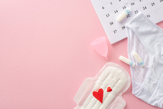Feminine hygiene supplies like pad with red hearts, symbolizing blood, tampons, menstrual cup, underpants, calendar marking the cycle start, on a pastel pink background with room for text or branding