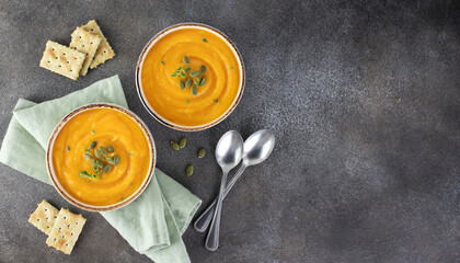 Pumpkin soup with creamy silky texture, pumpkin seeds, fresh thyme, croutons on brown background. Top view. Copy space.