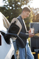 Caucasian man using smartphone and waiting power supply connect to electric vehicles for charging...
