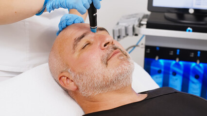 Close-up of a handsome young man getting facial rejuvenation therapy in a health spa