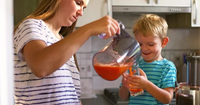 Mother pours freshly squeezed carrot juice into a glass for her child