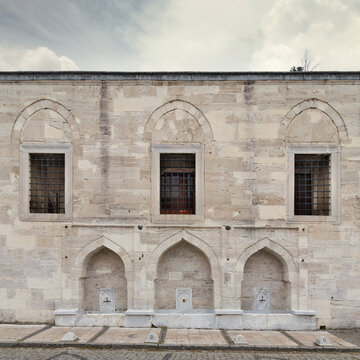 External stone wall of 16th century historic Atik Valide Mosque with row of ablution fountains and windows, located in Uskudar, Istanbul, Turkey, built by Nurbanu Sultan, the mother of Sultan Selim II