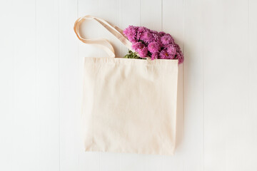 Tote bag mockup. Canvas bag with pink flowers lies on white wooden table. Eco shopping bag with...