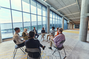 A diverse group of young business entrepreneurs gathered in a circle for a meeting, discussing...