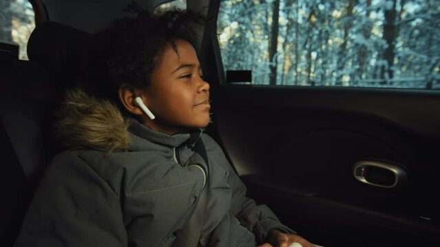 Side view of African American kid putting on earphones and bumping to beat while going somewhere by car