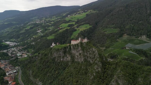 Klausen, Italy - 4K flying above Saben Abbey (Monastero di Sabiona) by Chiusa (Klausen) commune northeast of the city of Bolzano and South Tyrol Dolomites at the background on a cloudy summer day