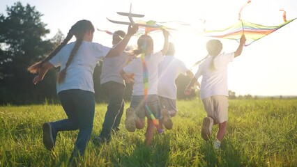 children run through the meadow in the park with toys in their hands. happy family kid dream concept. a group of little kids have fun together and play with flying kites toy airplane lifestyle