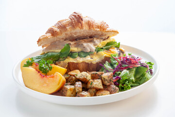 Brioche croissant scrambled egg Benedict with mushrooms and cream with sautéed potatoes and peach fruit.