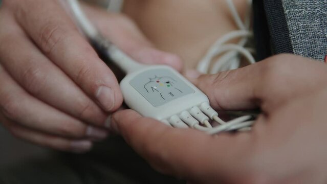 Man turns in his hands splitter of medical cardio device for measuring heart rhythm and ECG. Study of portable professional device for monitoring state of heart with scheme for attaching sensors.