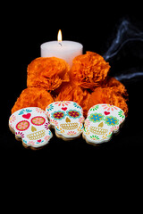 Cookies with shapes of catrinas and flowers with candle to celebrate Halloween or Day of the Dead on black background vertically