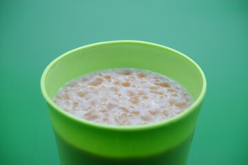 Green plastic cup containing cereal drink isolated on green background